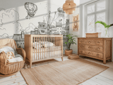 A children's room with a wooden crib, dresser, and chair, featuring a monochrome wall mural of a cityscape on the wall.