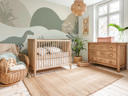 Dinosaur nursery mural wallpaper featuring soft-coloured dinosaurs, muted hills, and mountains, styled in a kids nursery with neutral wooden crib.