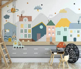 A colorful mural of a mini town with various buildings, a road, and decorative elements like clouds and stars, applied on a wall in a room with wooden furniture and a chalkboard.